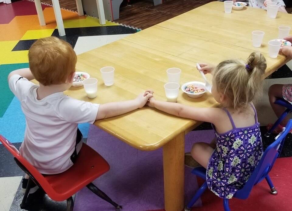 Two kids eating cereal while holding hands