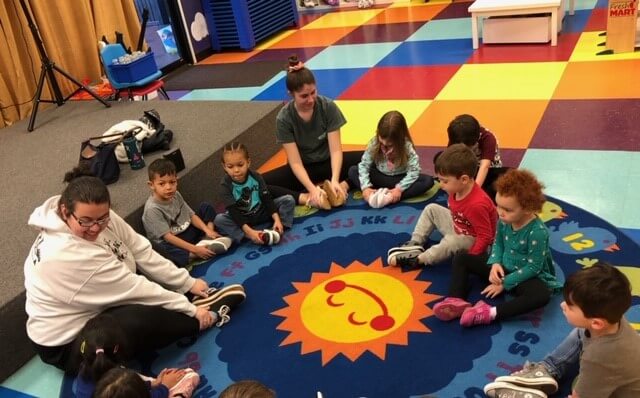 Preschool children on a carpet with their teacher.