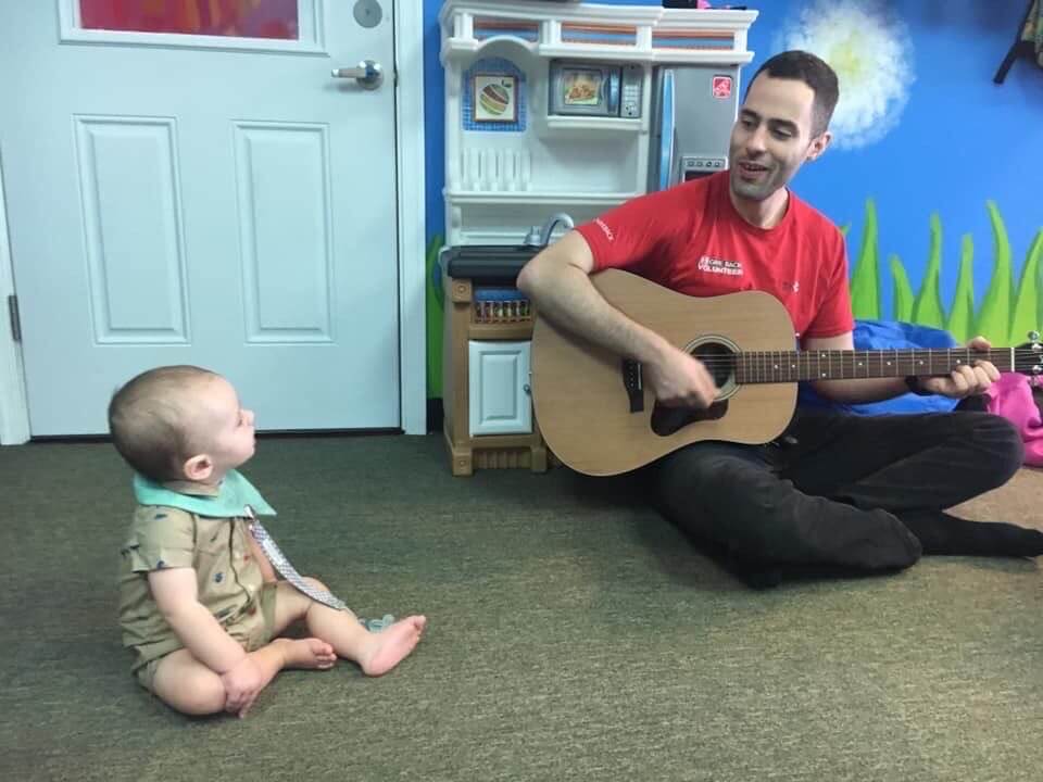 A man with a guitar with the baby watching