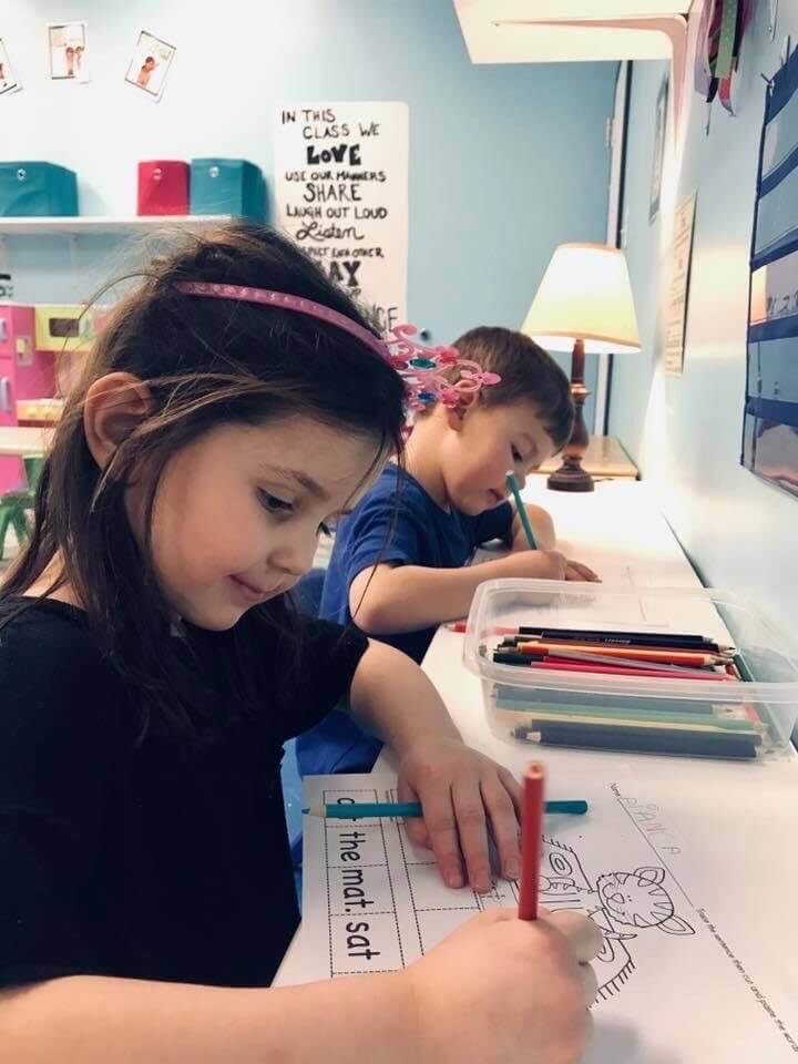 Two kids drawing cat in a piece of paper