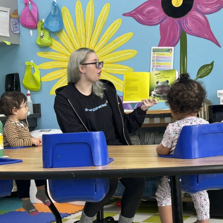 Teacher reading to toddlers in colorful classroom.