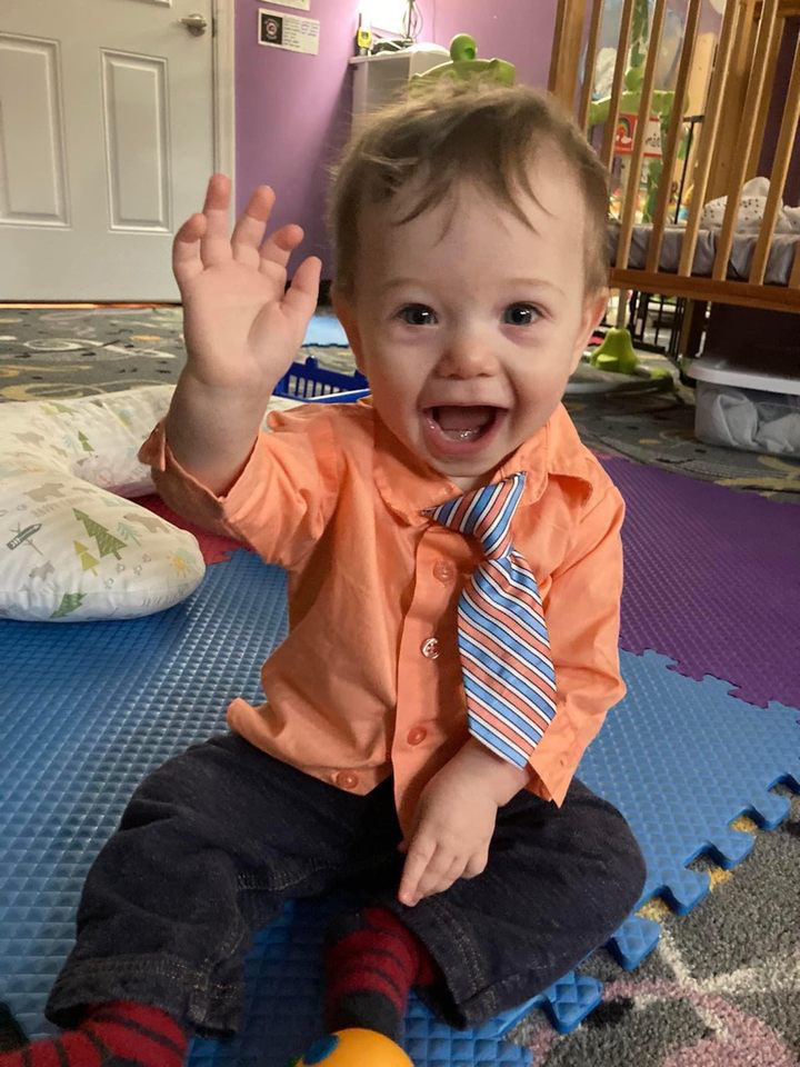 Smiling baby waving in colorful nursery.