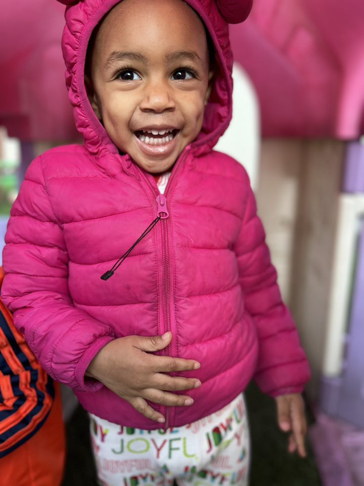 Smiling child in pink jacket indoors.