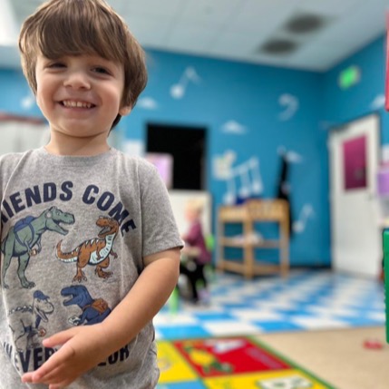Smiling child in dinosaur shirt at playroom.