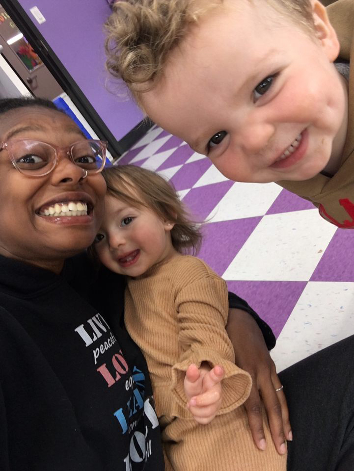 Smiling group selfie with children on purple floor.