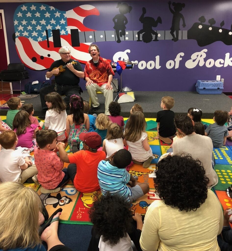 Musicians perform for children in colorful classroom.