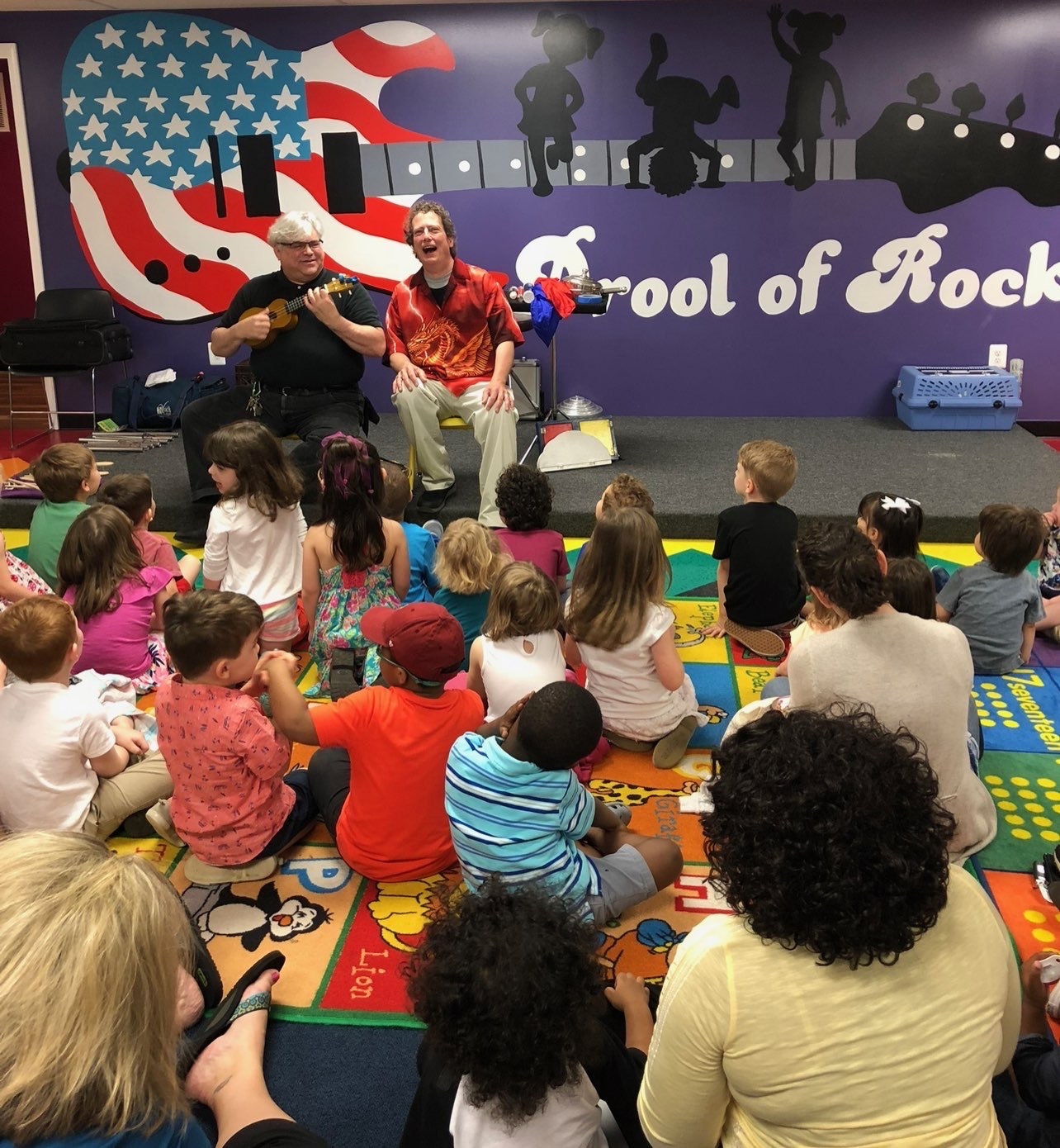 Musicians perform for children in colorful classroom.