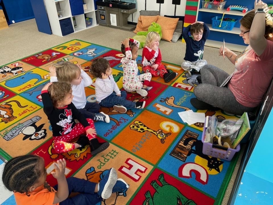 Teacher reading to children on colorful play rug.