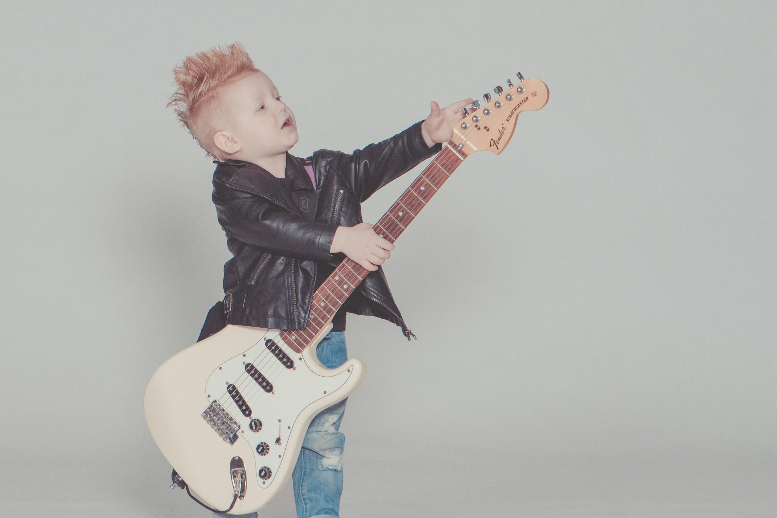 Stylish young boy with a mohawk strumming an electric guitar, wearing a leather jacket and blue jeans at a childcarecenter in owings mills