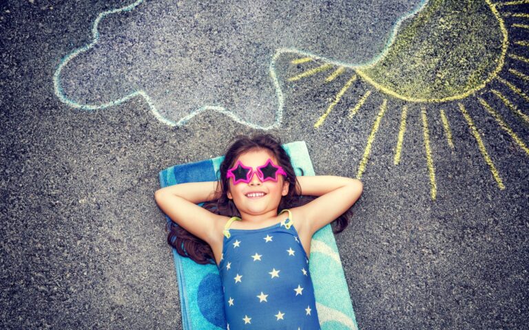 Little girl laying on a beach towel in the preschool yard. Activities for Daycare