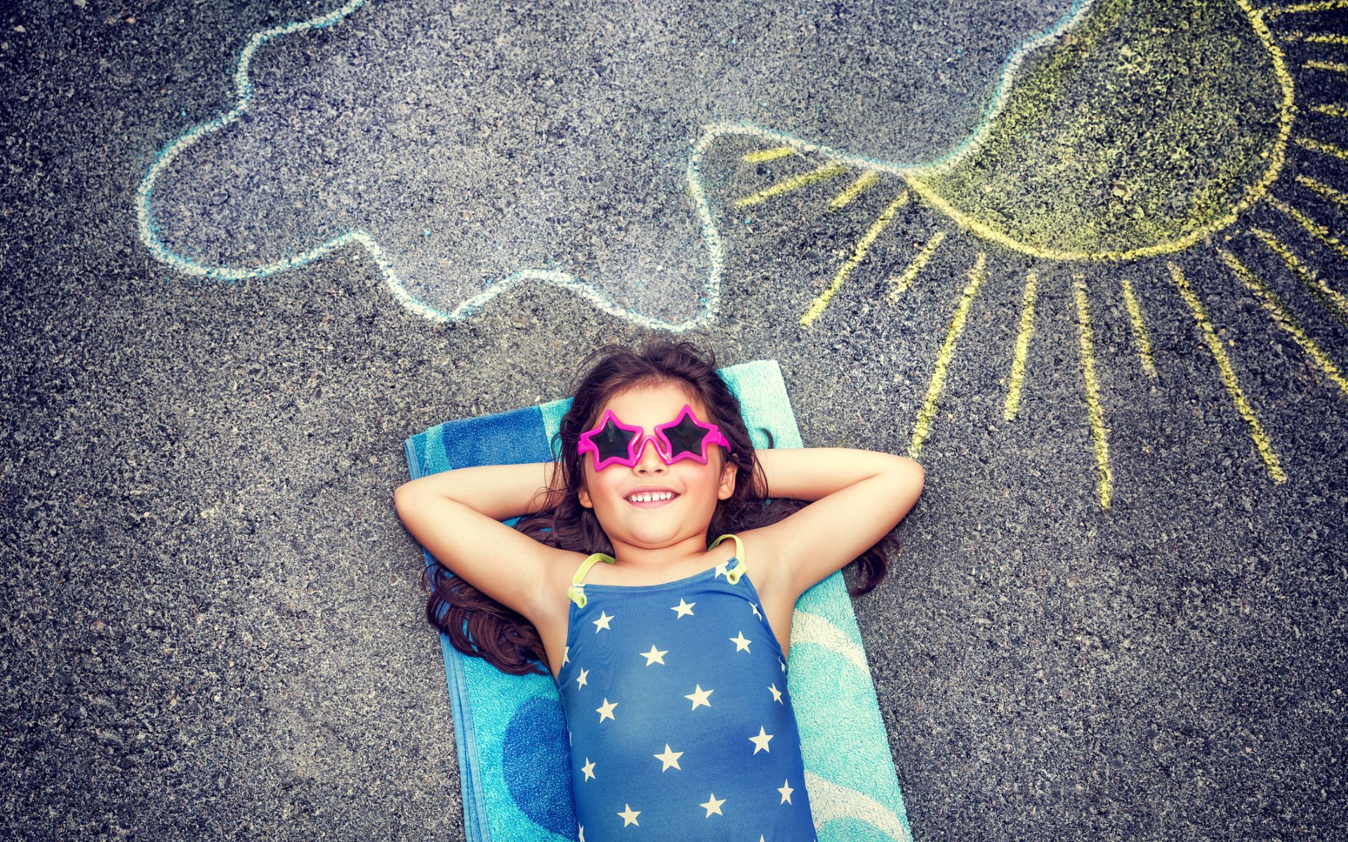 Little girl laying on a beach towel in the preschool yard. Activities for Daycare